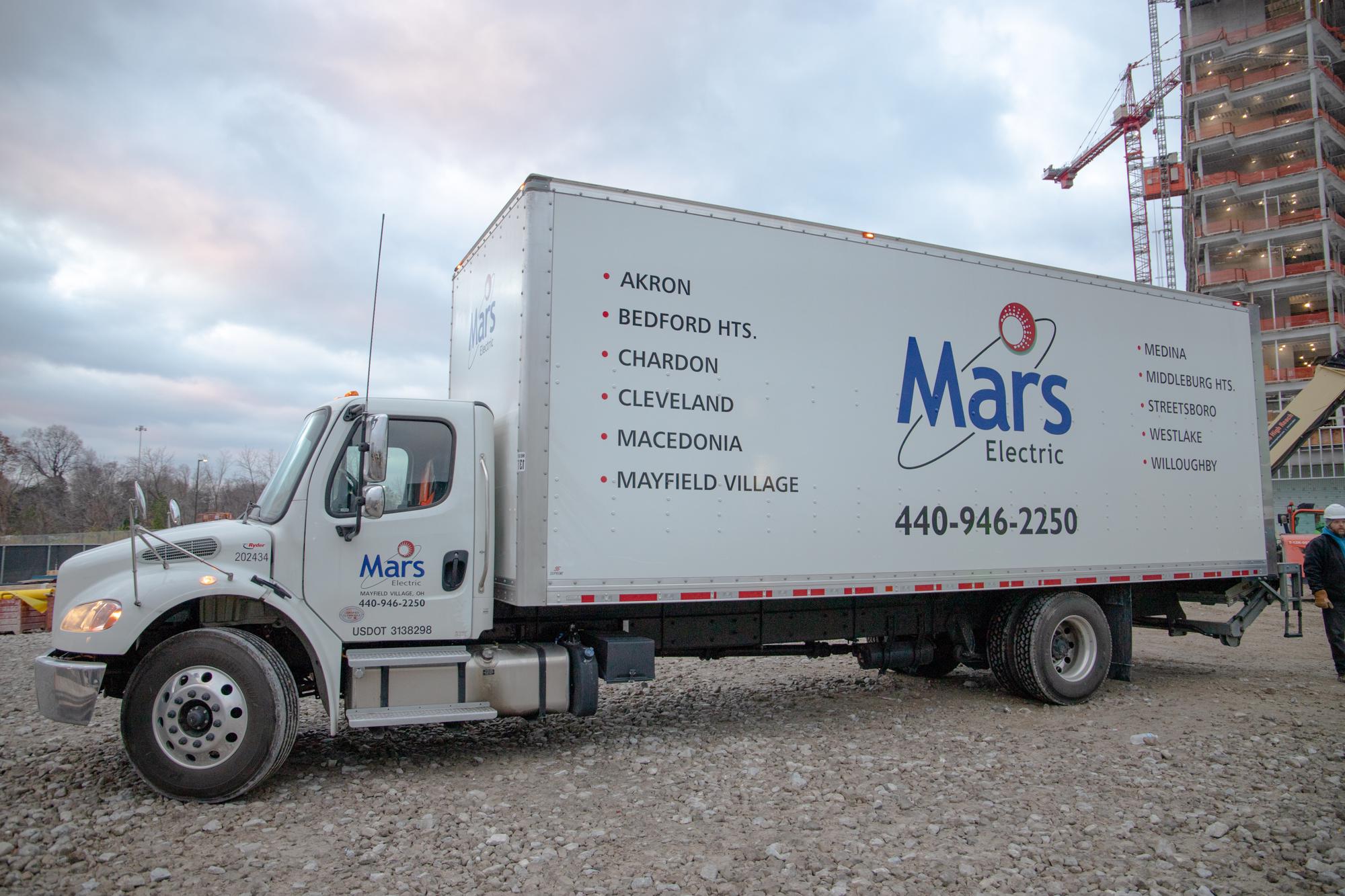 A Mars Electric delivery truck parked at a skyscraper being built